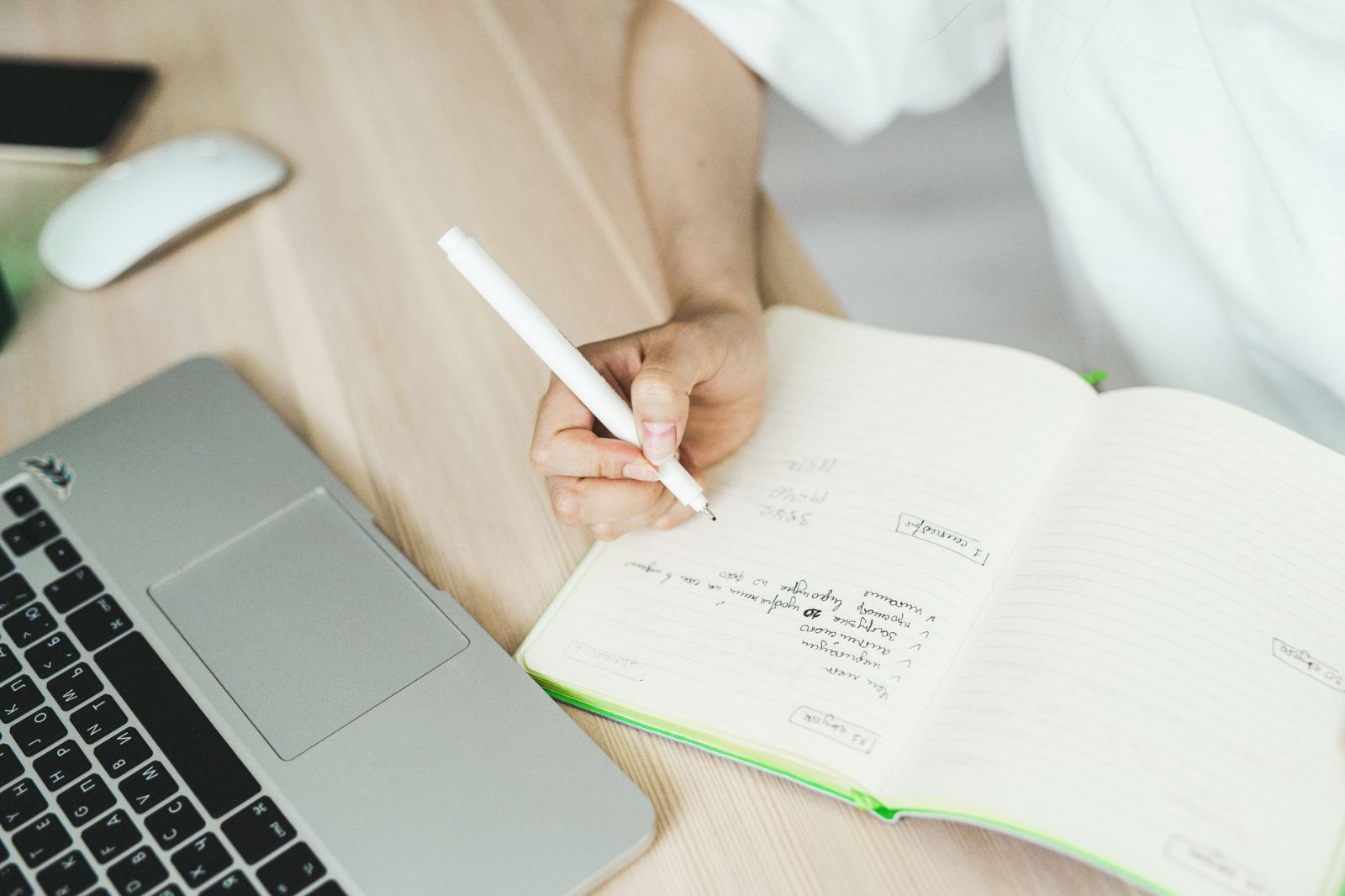 An open notebook or printed template lying beside the keyboard with a short handwritten plan visible — entry, exit and risk noted in pen — the chart's glow at the edge of frame, mug and pen present, same desk and same warm side light as the hero